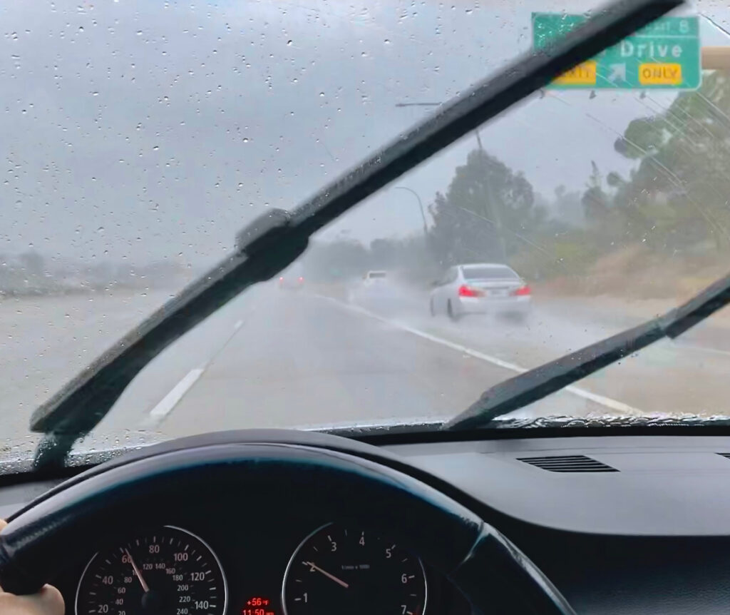 Driver’s view through a windshield in heavy rain with wipers on and low visibility on a wet highway.