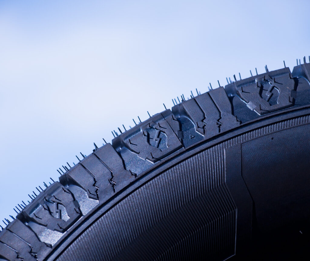 Close-up of a car tire showing detailed tread pattern and texture against a light blue background.