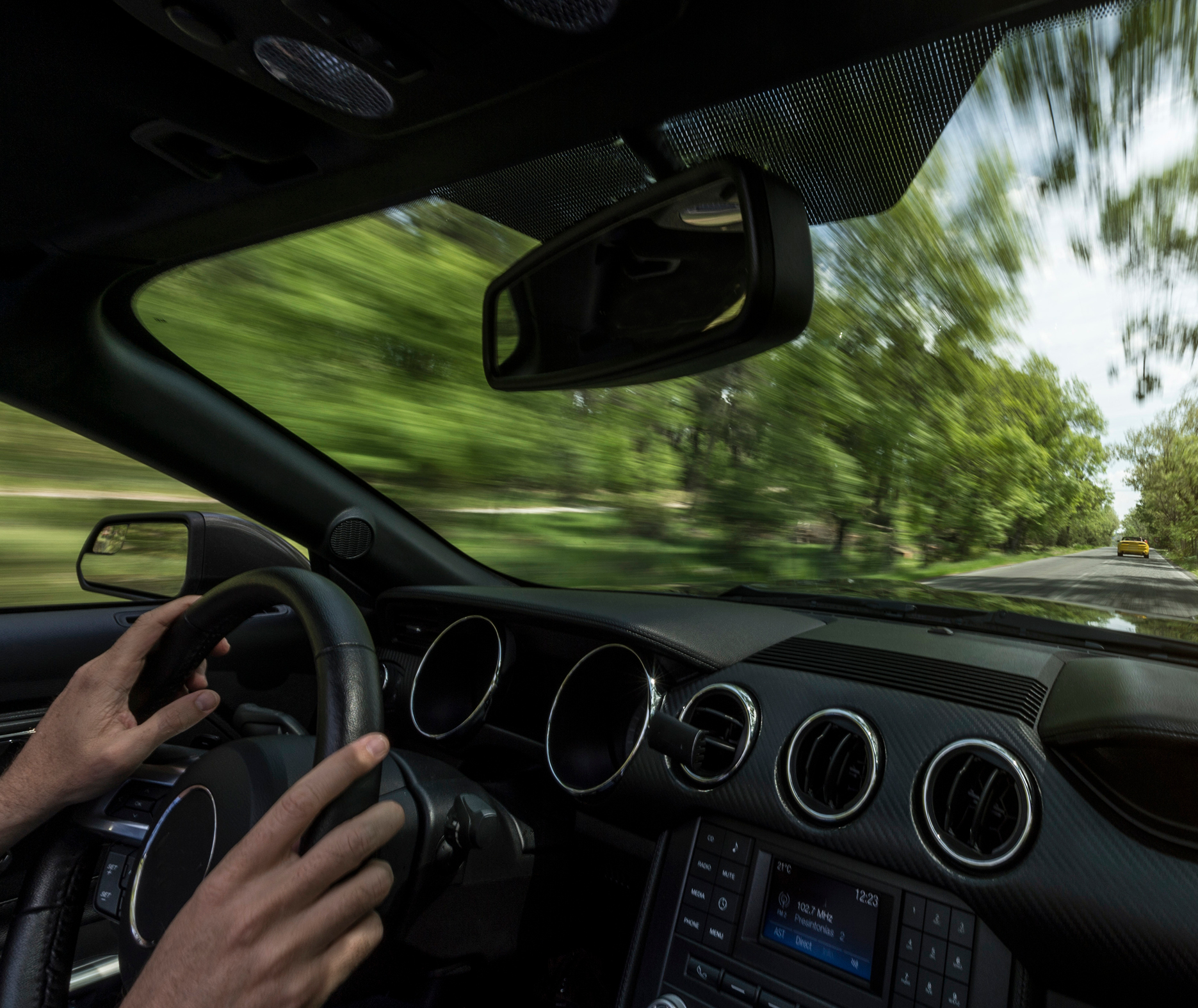 Driver's view from inside a car with both hands on the steering wheel on a tree-lined road