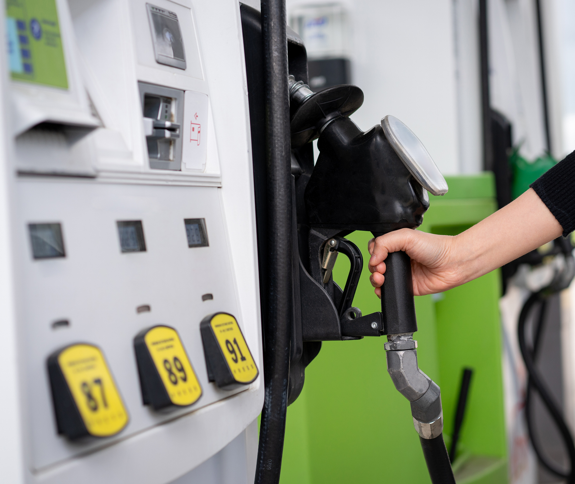 Hand lifting a fuel nozzle from a gas pump with 87, 89 and 91 octane buttons