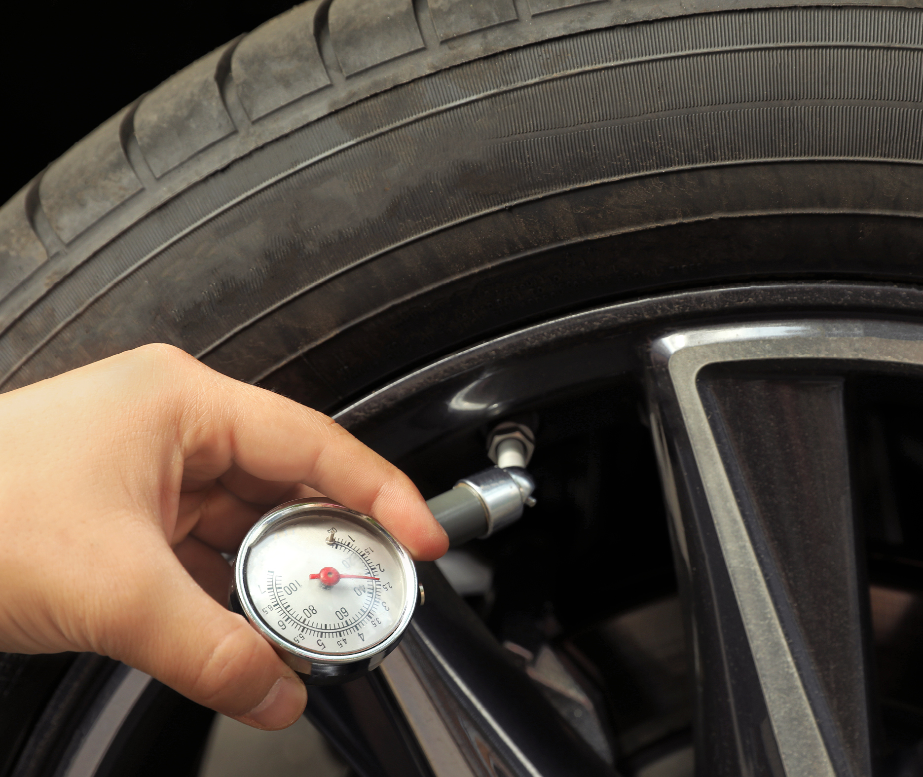 Hand checking car tire pressure with an analog gauge on the valve stem