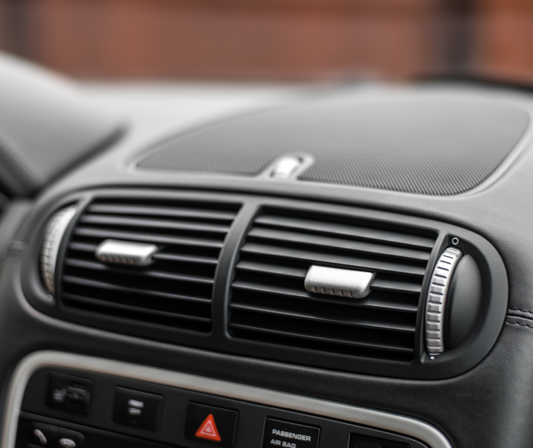 Close-up of central air vents on a car dashboard with a leather-trimmed interior